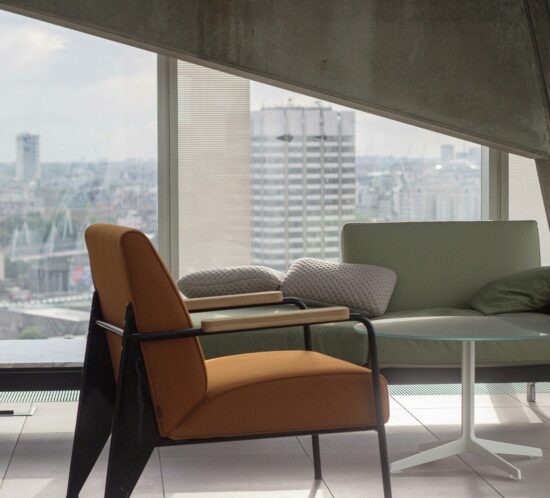 Modern seating area with orange chair and glass table, cityscape visible through large windows.